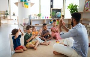 Nursery school children with man teacher sitting on floor indoors in classroom, playing.